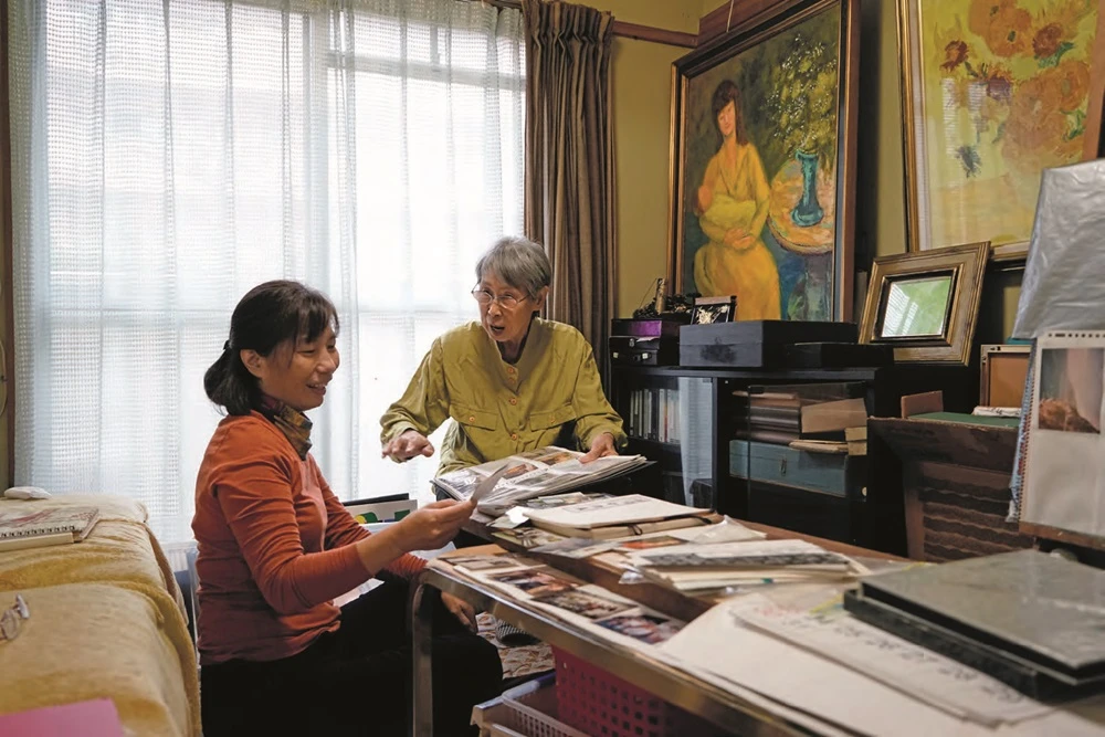鄭瓊娟和筆者（左）解說老照片與保存的剪報。鄭瓊娟的剪貼簿，貼滿1970 年代日本新聞社和公家美術館合辦的西洋美術大展作品與介紹文字。-圖片
