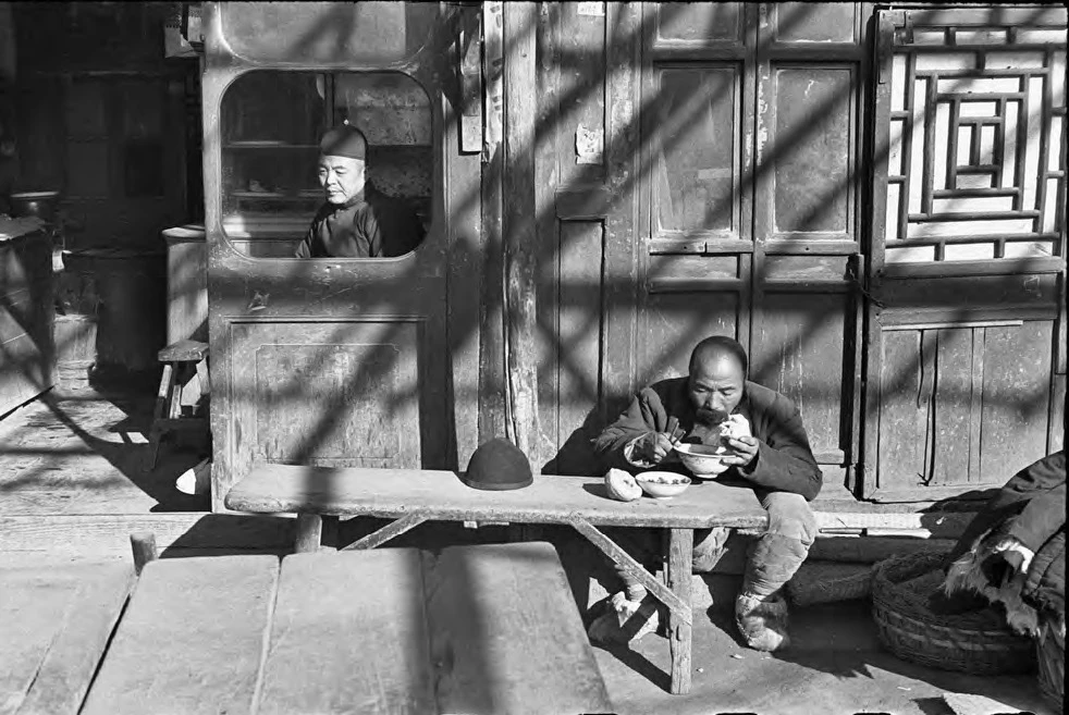 坐在食肆窗內的跑堂或店主，苦力在簷下用餐，北平，1948年12月。©Fondation Henri Cartier-Bresson / Magnum Photos-圖片