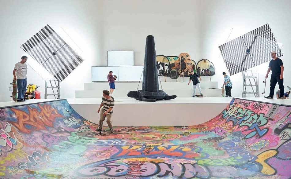 背景作品：（左1、右1） Liam Morgan，《Meaningless Bound Form no.2》、《Meaningless Bound Form no.1》，螢光燈管、鋼、馬達，2022；（左2） 三頻道錄像；（中）象徵宇宙龜（The cosmic tortoise） 及須彌山（Mount Meru）的大型充氣偶 交織羅摩衍那神話及格林童話故事、並以乳牛皮製作成的泰國皮影戲偶（Nang Yai）；攝影：Nicolas Wefers；來源：文件展官網-圖片