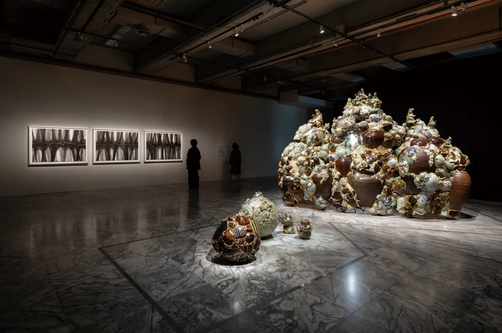 圖右側為李受俓（Yeesookyung），《轉譯瓷瓶_何時再見_2025》（<i>Translated Vase_When Will I See You Again_2025</i>），2025，陶瓷碎片、鋼、環氧樹脂、24K 金箔、燈光，275 （高）×387×155公分，藝術家版權所有，由 2025台北雙年展委託製作。本作品之國際運輸承蒙 KOFICE 慷慨支持。本作品之製作經費亦承蒙 Iljin Cultural Foundation 慷慨支持。圖左側為金玟廷（Minjung Kim），《位移》（<i>Phasing</i>），2025，墨水、韓紙，三聯幅，每幅 99×139公分，藝術家版權所有。本作品承蒙 Studio Minjung Kim 慷慨支持，得以實現。2025台北雙年展現場；呂國瑋攝影。-圖片